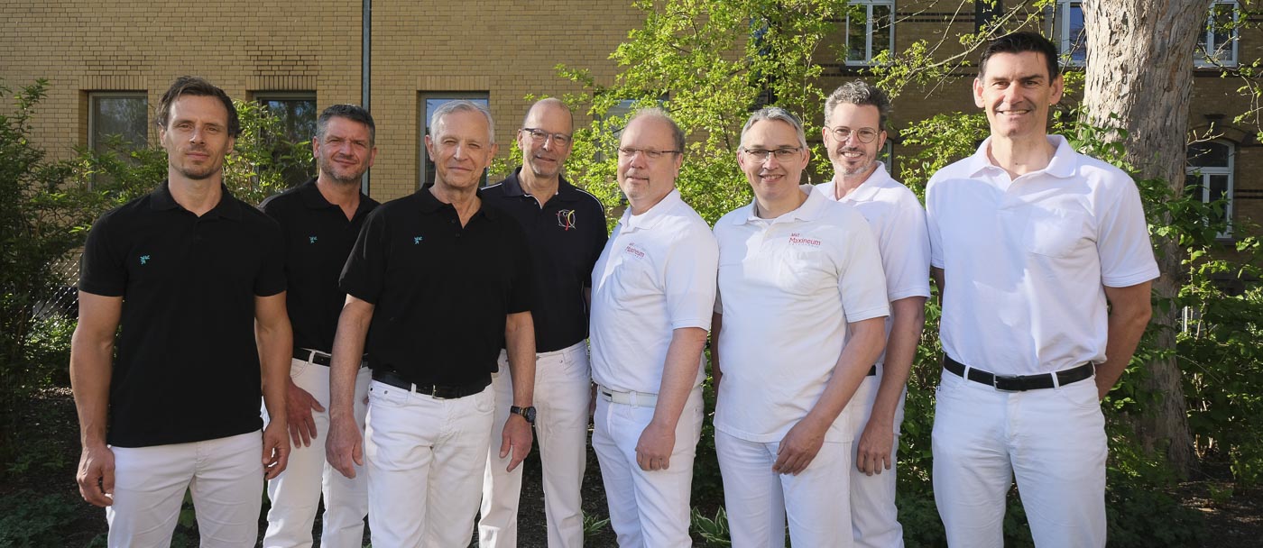 Eine Gruppe von acht Männern in weißen und schwarzen Hemden draußen vor einem Gebäude.