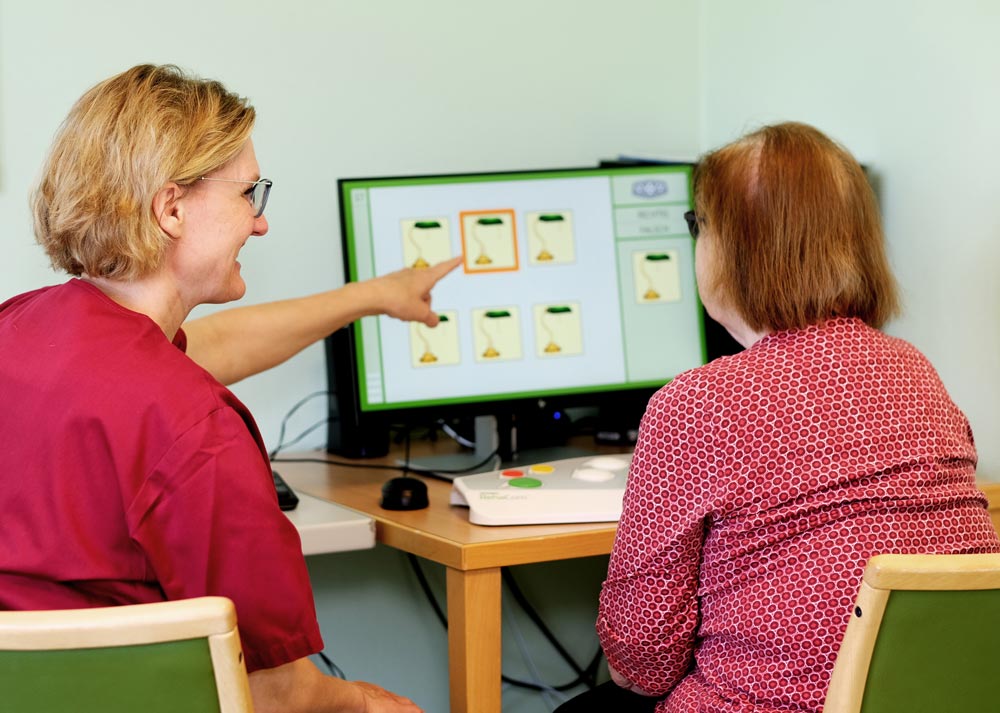 Zwei Frauen sitzen vor einem Computerbildschirm, auf dem Karten mit Bildern angezeigt werden. Eine zeigt auf den Bildschirm.