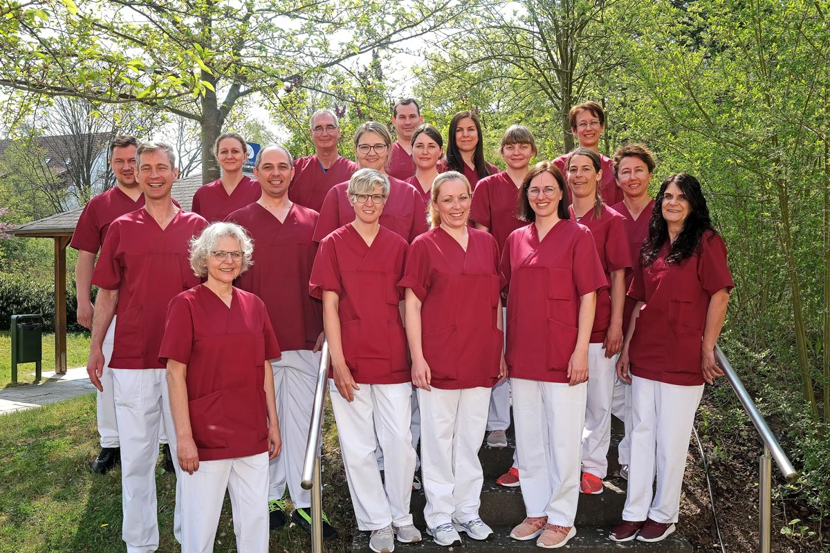 . Eine Gruppe von Menschen in roten Kitteln steht draußen auf einer Treppe, umgeben von Bäumen.