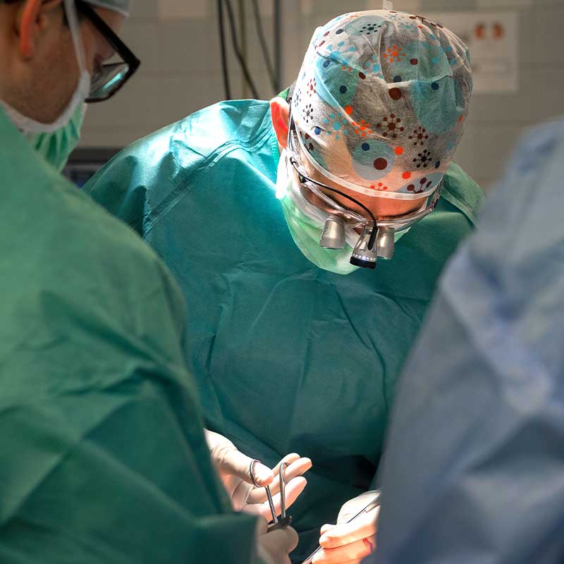 Chirurgen im OP-Saal, konzentriert bei der Arbeit mit Instrumenten und Lupenbrillen.