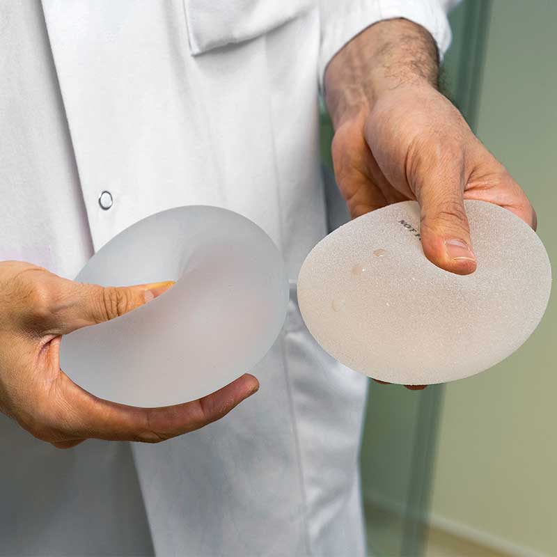 Eine Person hält zwei Brustimplantate in den Händen, gekleidet in einen weißen Kittel.