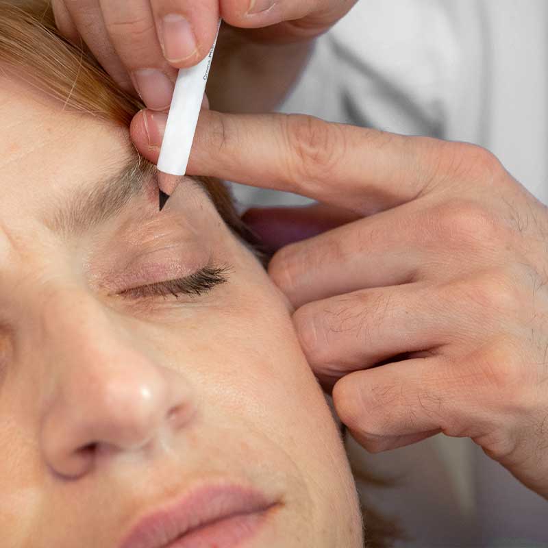 Eine Person bekommt ihre Augenbrauen mit einem Stift gezeichnet.