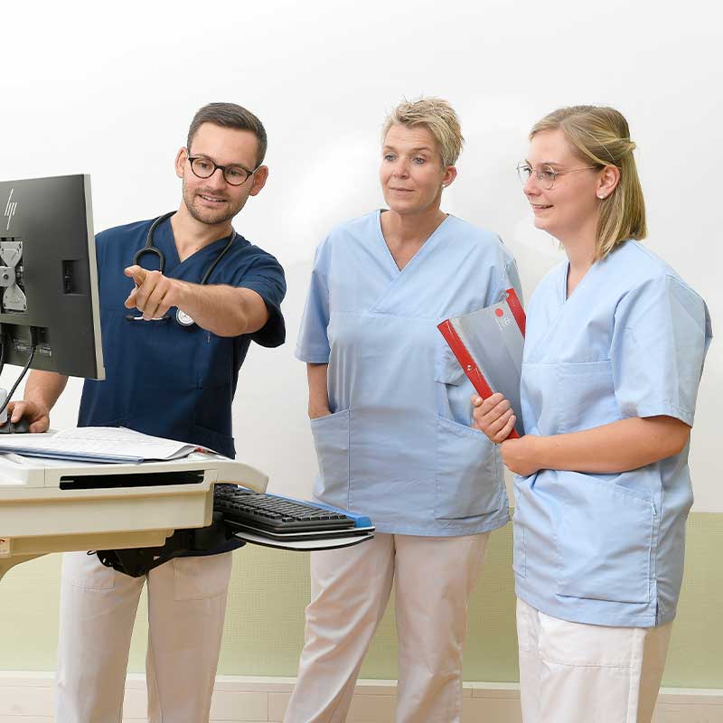 Drei medizinische Fachkräfte in Uniformen stehen vor einem Computer, einer zeigt auf den Bildschirm.
