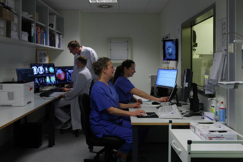 Ärzte und Pflegepersonal in blau arbeiten an Computern und überwachen medizinische Scans in einem Krankenhausbüro.