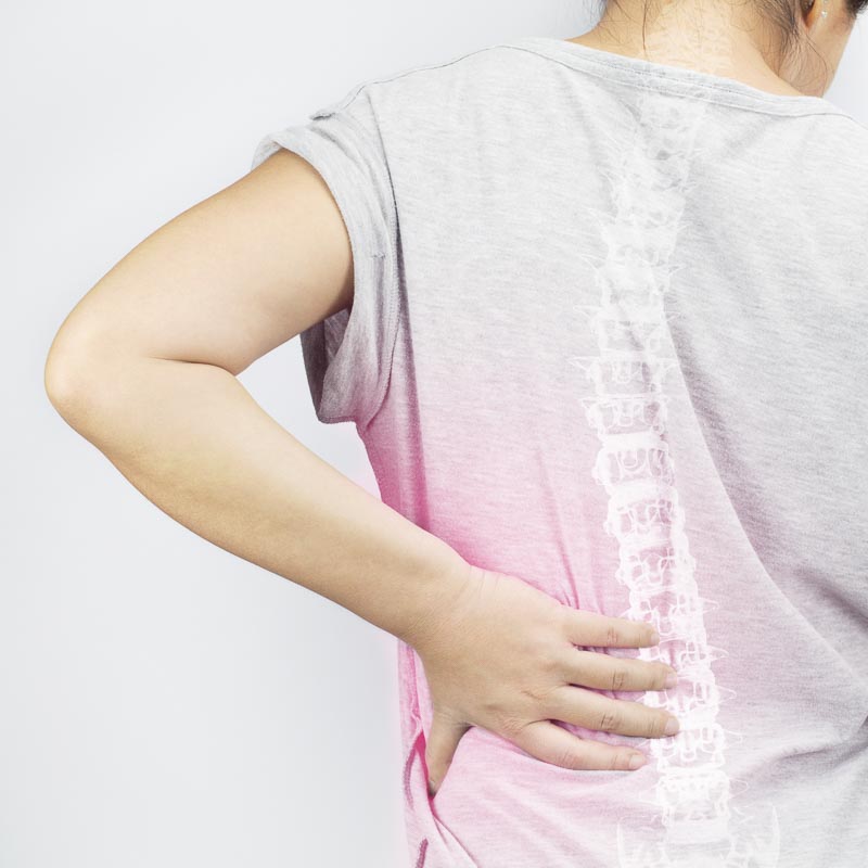 Eine Person hält ihren schmerzenden unteren Rücken, mit einer Röntgenaufnahme der Wirbelsäule auf dem T-Shirt.