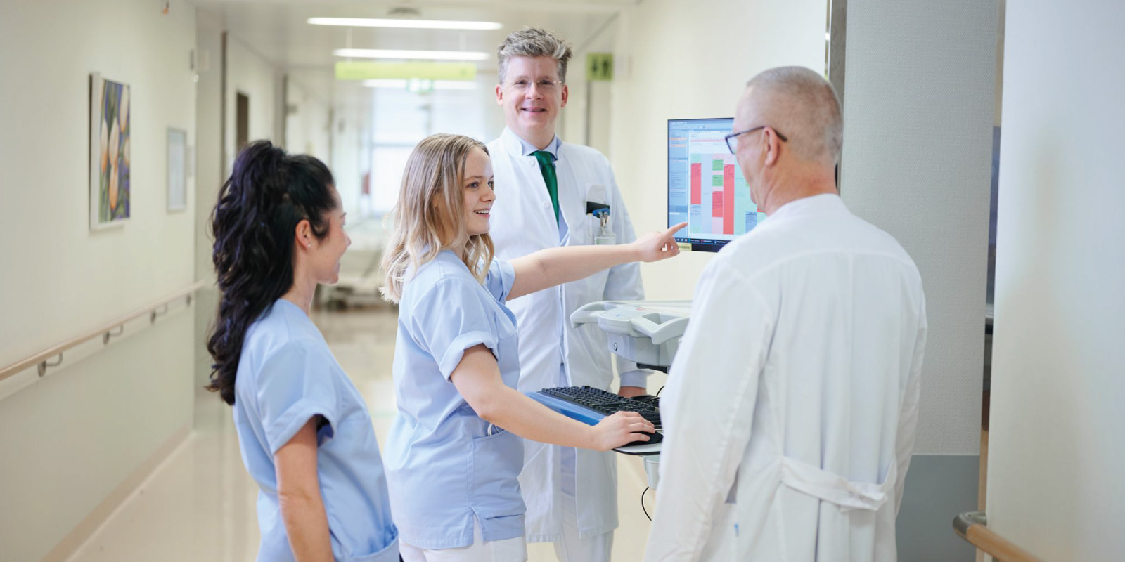 Ärzte und Krankenschwestern in einem Krankenhausflur schauen auf einen Monitor und besprechen Daten.