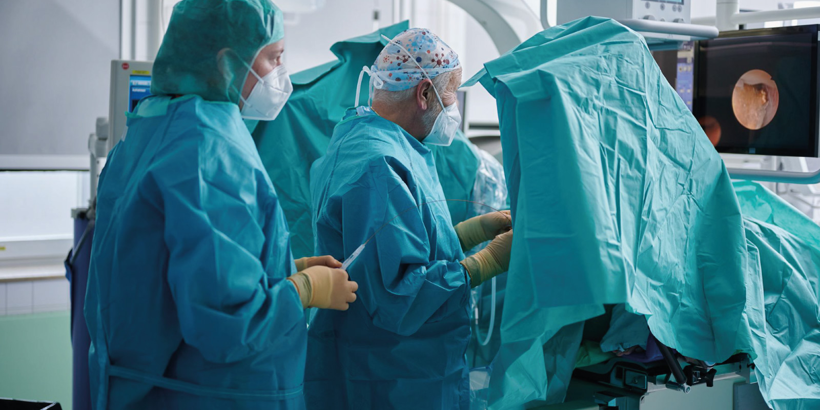 Ärzte in OP-Kleidung führen eine Operation durch, während sie einen Monitor in einem sterilen OP-Raum beobachten.