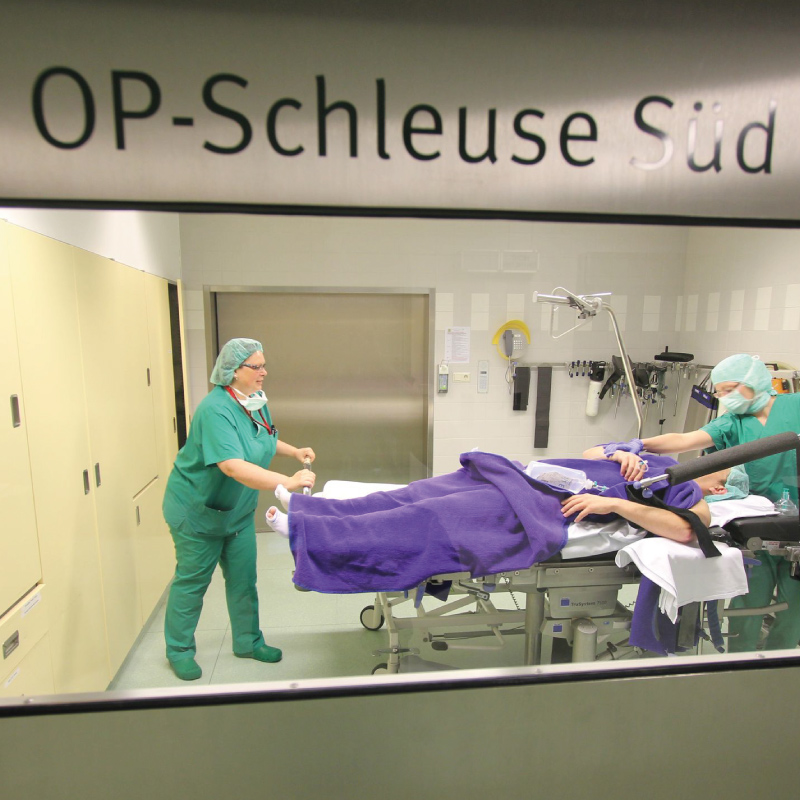 Krankenhaus-OP-Szene: Personal in grüner OP-Kleidung bereitet Patienten auf den Eingriff im "OP-Schleuse Süd" vor.