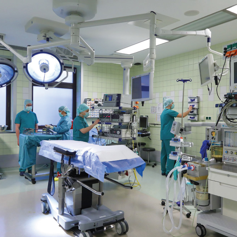 Krankenhaus-Operationssaal mit medizinischen Geräten und Personal in grüner OP-Kleidung, das sich auf eine Operation vorbereitet.