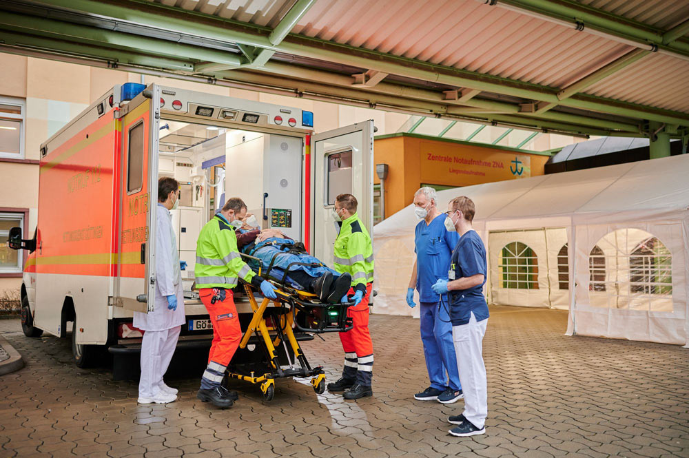 Mitarbeiter laden einen Patienten aus einem Krankenwagen vor einer Notaufnahme aus.