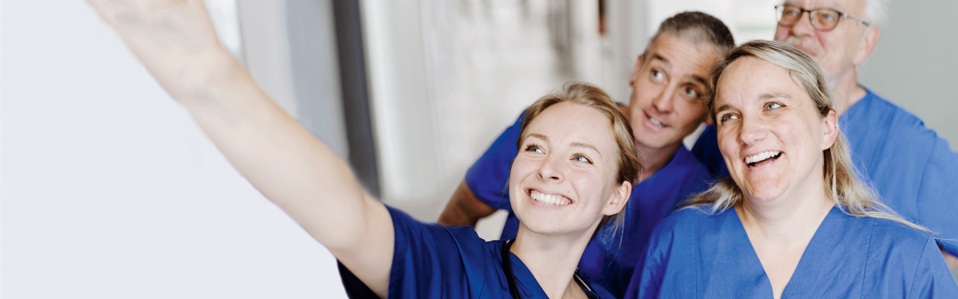 Eine Gruppe von medizinischem Personal in blauen Kitteln macht ein Selfie und lächelt.