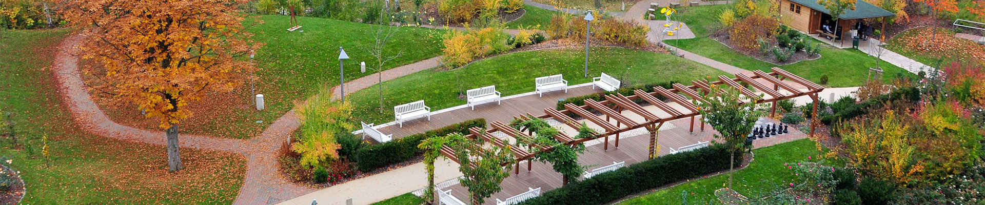 Ein Herbstpark mit Gehwegen, Bänken, Pavillon, großen Bäumen und Schachbrett.