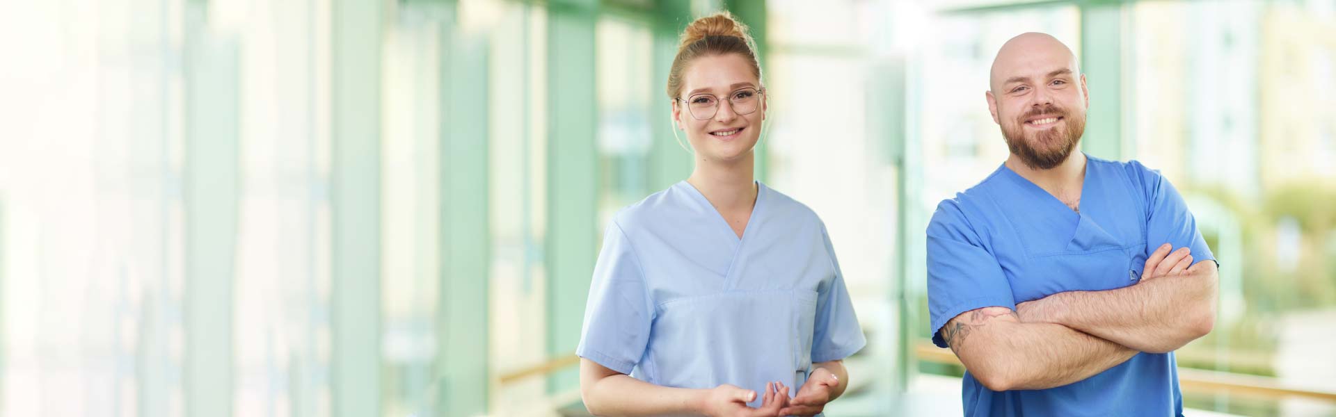 Zwei Personen in blauer Arzthelferkleidung lächeln in einem hellen Raum.