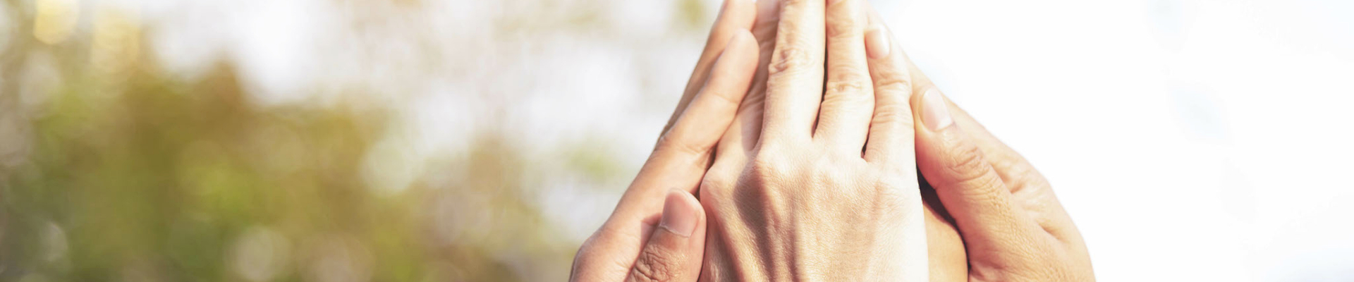 Zwei Hände halten sich sanft vor einem verschwommenen, natürlichen Hintergrund.