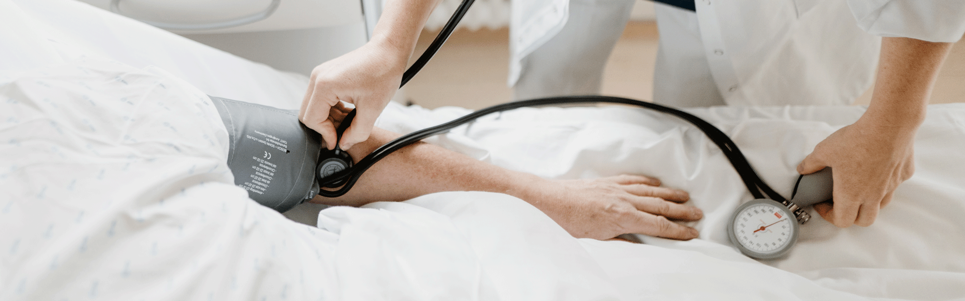 Eine Person misst mit einem Blutdruckmessgerät den Blutdruck eines Patienten im Bett.