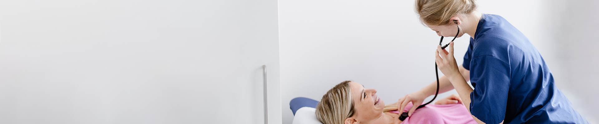 Eine Ärztin untersucht eine lächelnde Patientin im Krankenhaus mit einem Stethoskop.