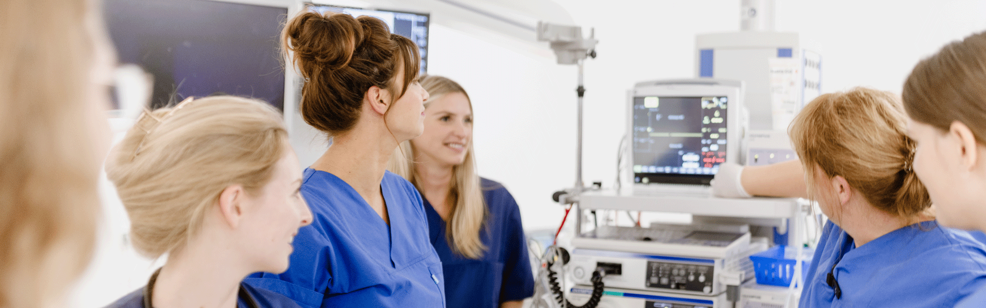 Krankenschwestern in blauen Kitteln betrachten ein medizinisches Gerät in einem Krankenhausraum.
