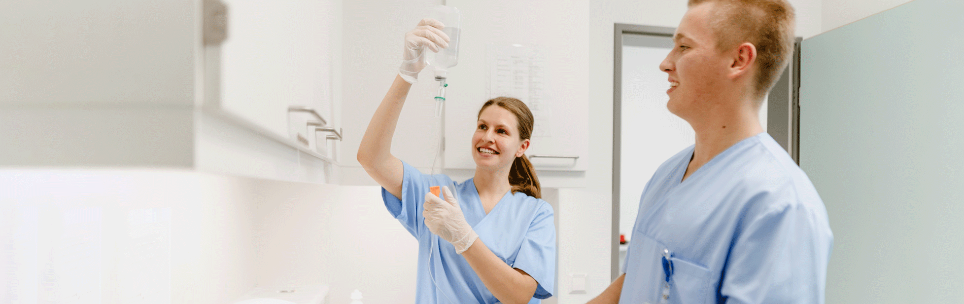 Krankenhauspersonal in blauer Kleidung prüft intravenöse Lösung in medizinischem Raum.