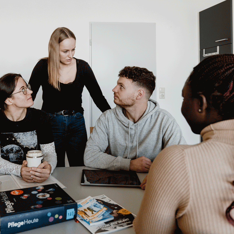 Vier Personen diskutieren an einem Tisch mit einem Buch und Zeitschriften.