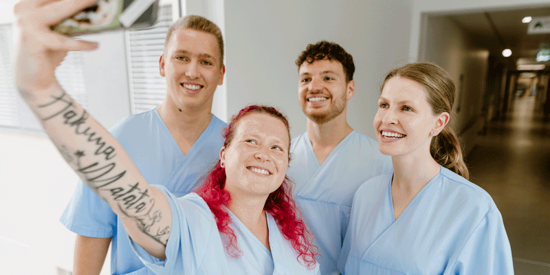 Vier Personen in medizinischer Kleidung machen ein Selfie und lächeln.