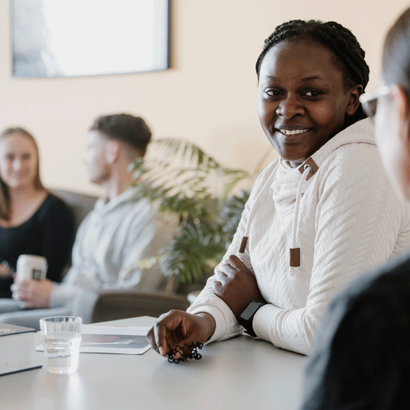 Eine Gruppe von Personen in einem Meeting, lächelnd, mit Pflanzen und Getränken auf einem Tisch.