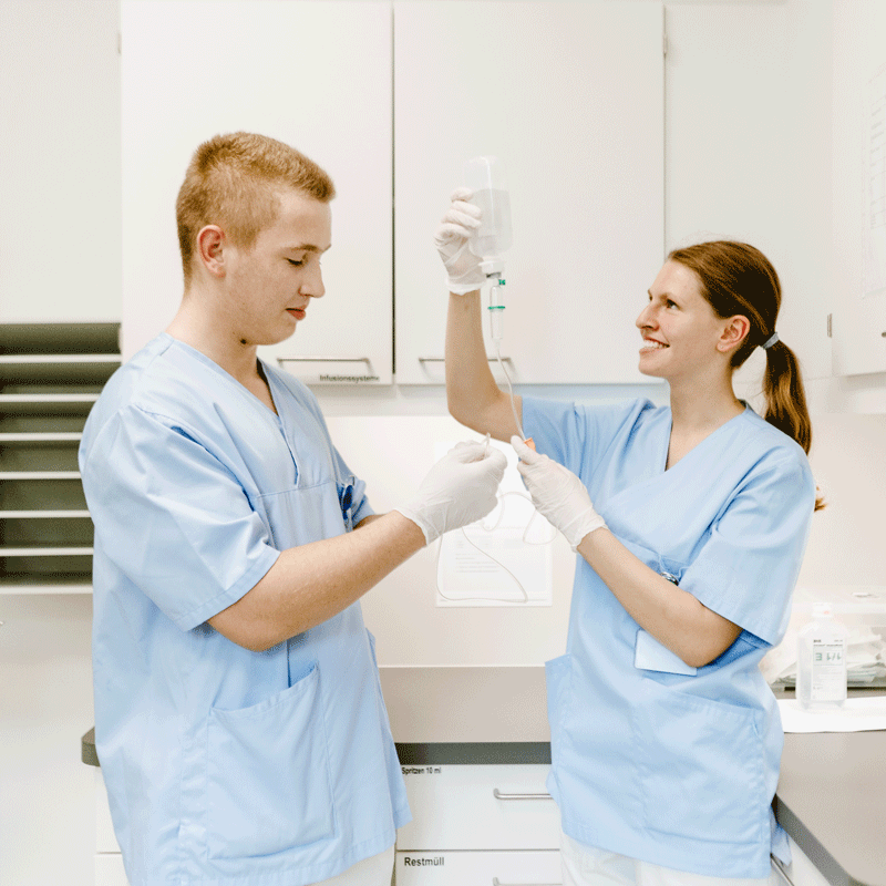 Zwei Krankenhausmitarbeiter in blauen Kitteln bereiten eine Infusion vor.