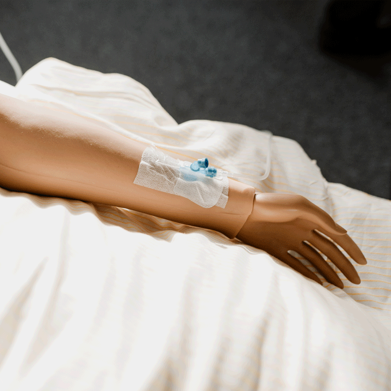 Kunstarm mit intravenösem Zugang, liegt auf einem weißen Bettlaken.