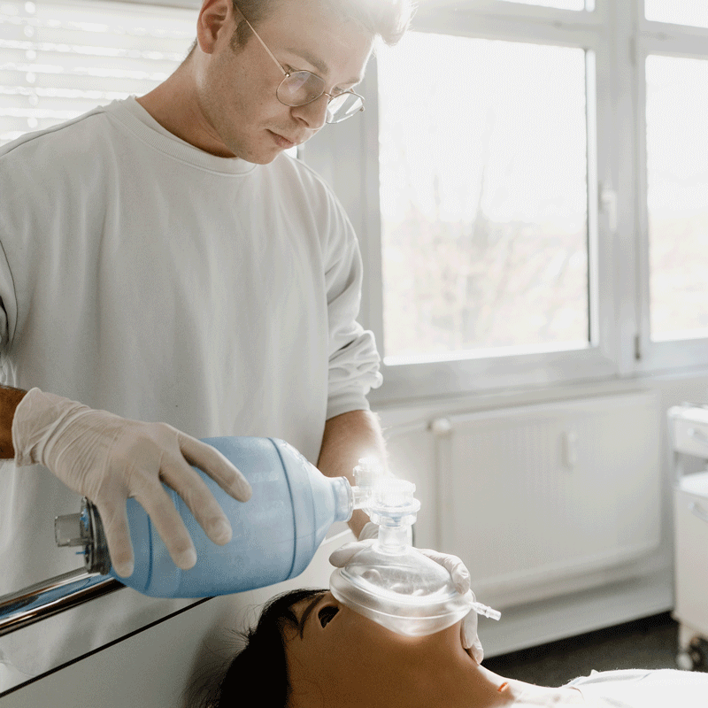 Person mit Handschuhen übt an Puppe Reanimation mit Beatmungsbeutel in einem hellen Raum.