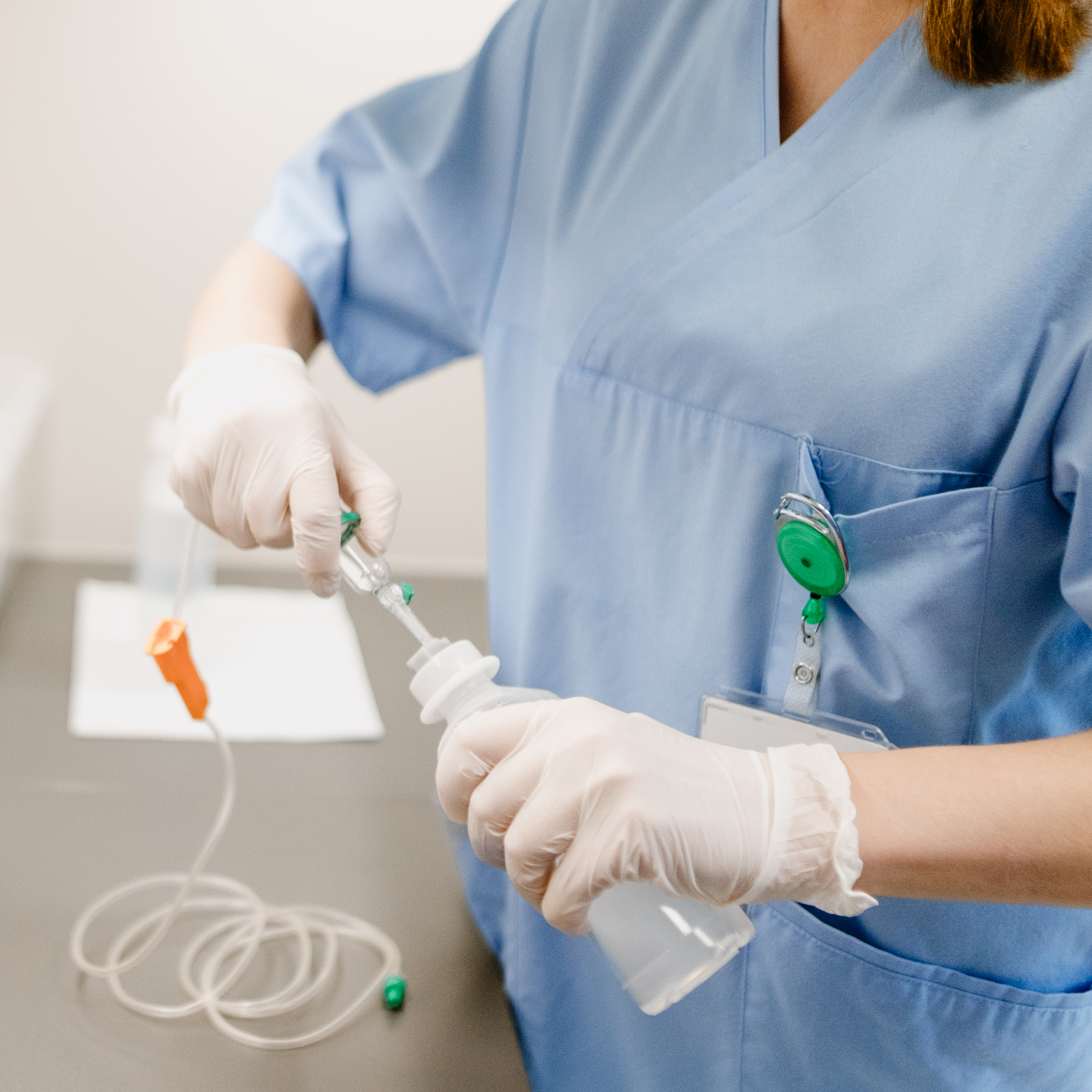 Eine Pflegekraft in blauer Uniform bereitet eine medizinische Flüssigkeit mit Handschuhen und Schlauch vor.