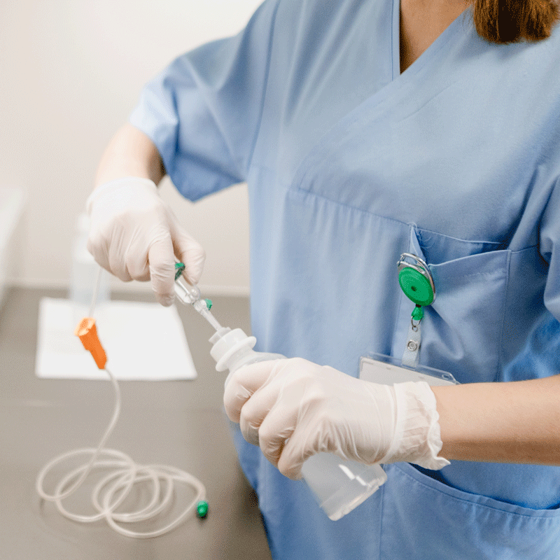 Eine Person in blauer medizinischer Kleidung bereitet eine Infusion vor, mit Handschuhen und Infusionsset.