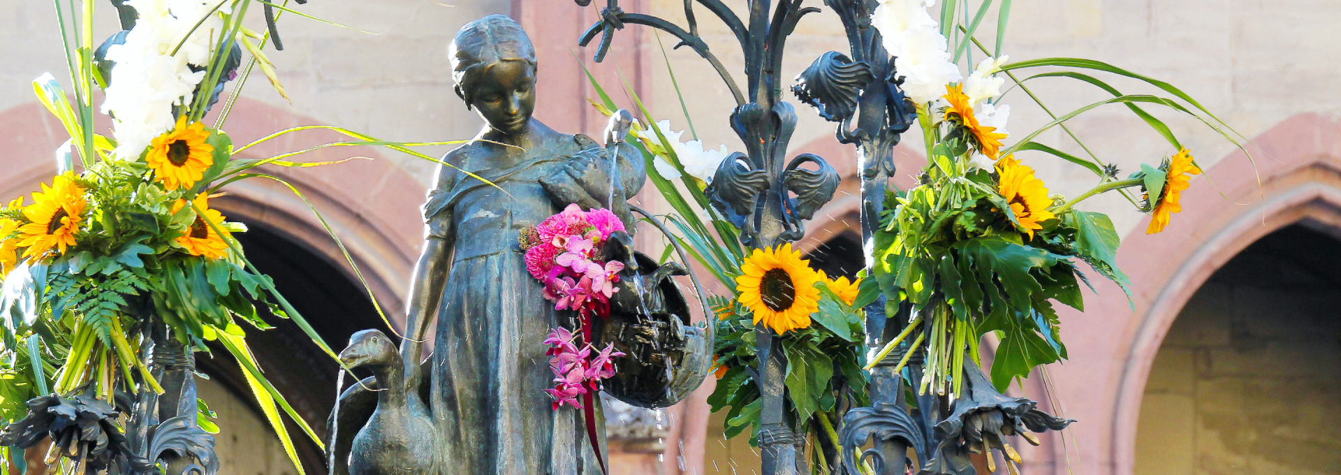 Eine Statue eines Mädchens mit Blumen und Sonnenblumen, umgeben von dekorativen Pflanzen.