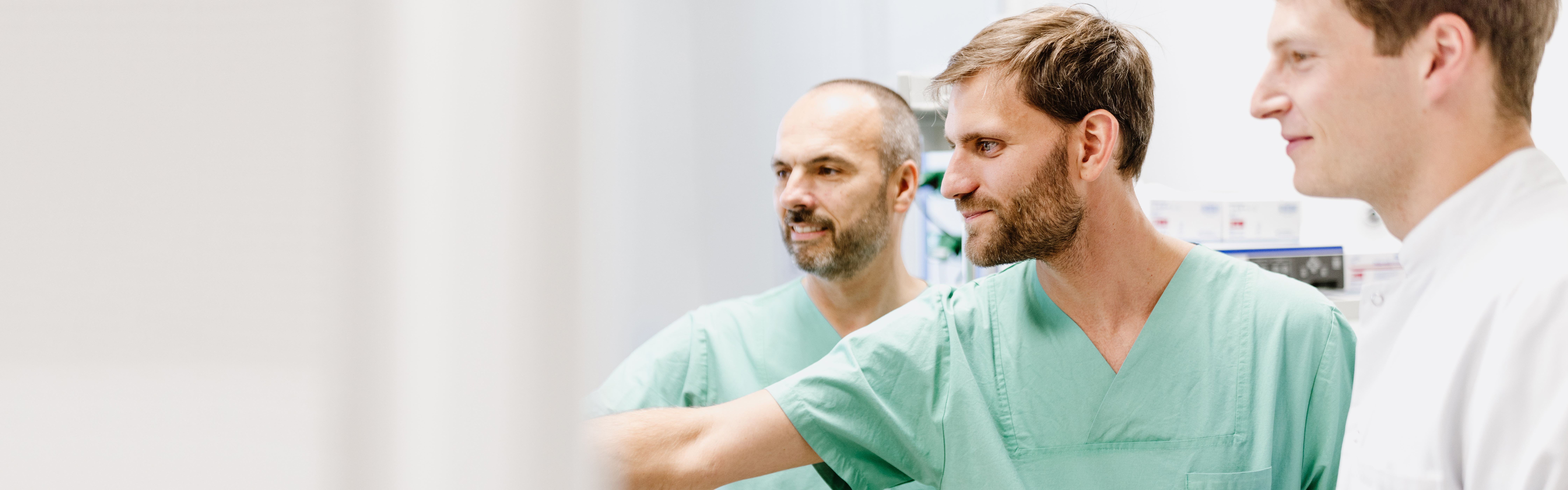 Drei Ärzte in grüner Kitteln arbeiten zusammen in einem medizinischen Umfeld.