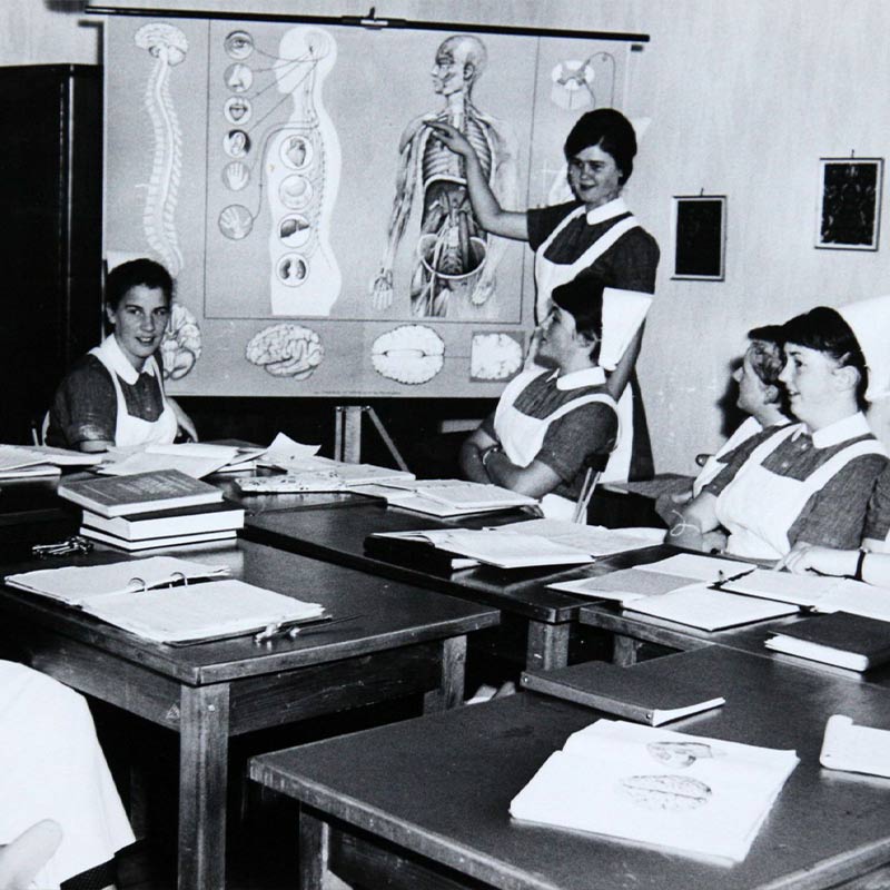 Eine Gruppe von Krankenschwestern in Uniform studiert eine anatomische Darstellung in einem Klassenzimmer.