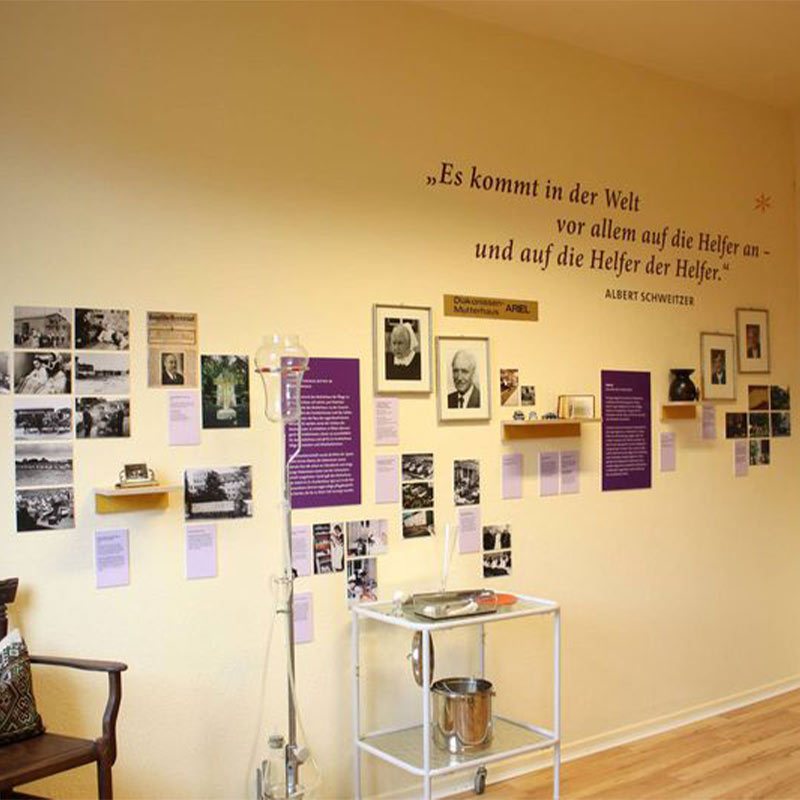 Eine Wand mit Fotos, Zitaten und medizinischem Gerät. Zitat von Albert Schweitzer über Helfer.
