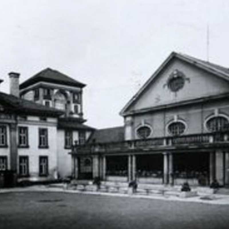 Ein historisches Foto eines alten Gebäudes mit einer Veranda und Fenstern, architektonische Details erkennbar.