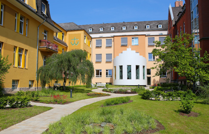 Ein schöner Innenhof mit Garten, modernen Gebäuden und Bäumen bei sonnigem Wetter.