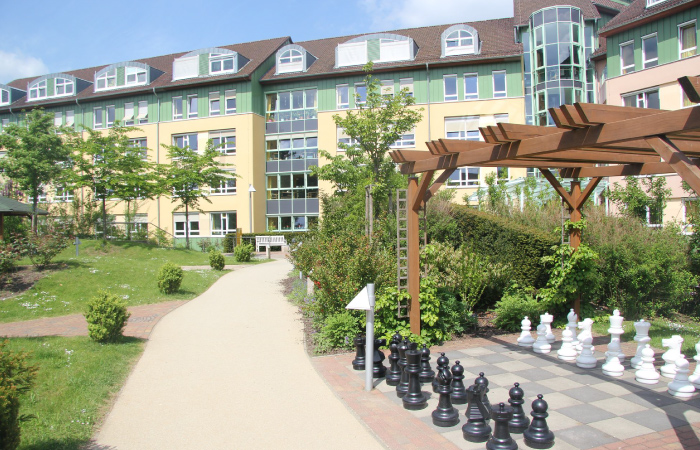 Ein großer Gebäudekomplex mit Garten, Gehweg und einem großen Schachbrett unter einer Pergola.