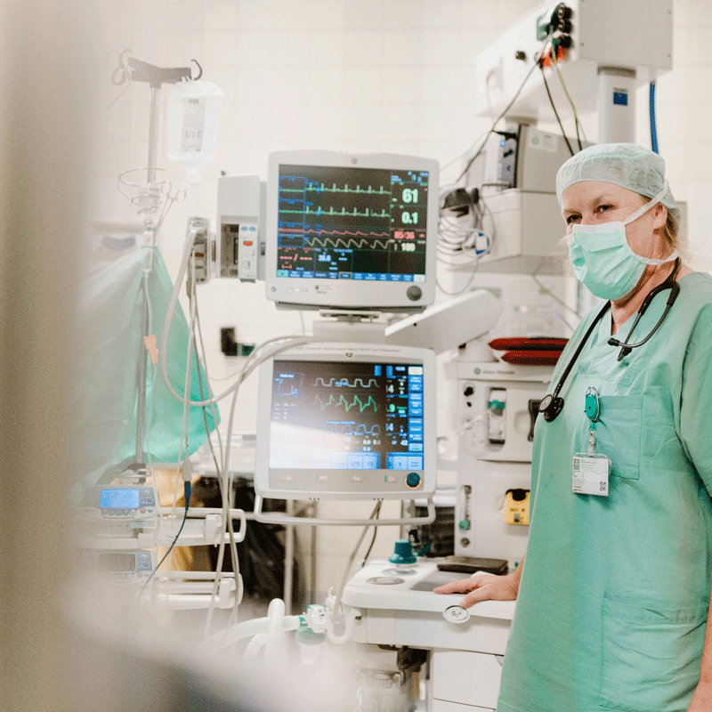 Ein Arzt in OP-Kleidung steht neben medizinischen Überwachungsgeräten im Krankenhaus.