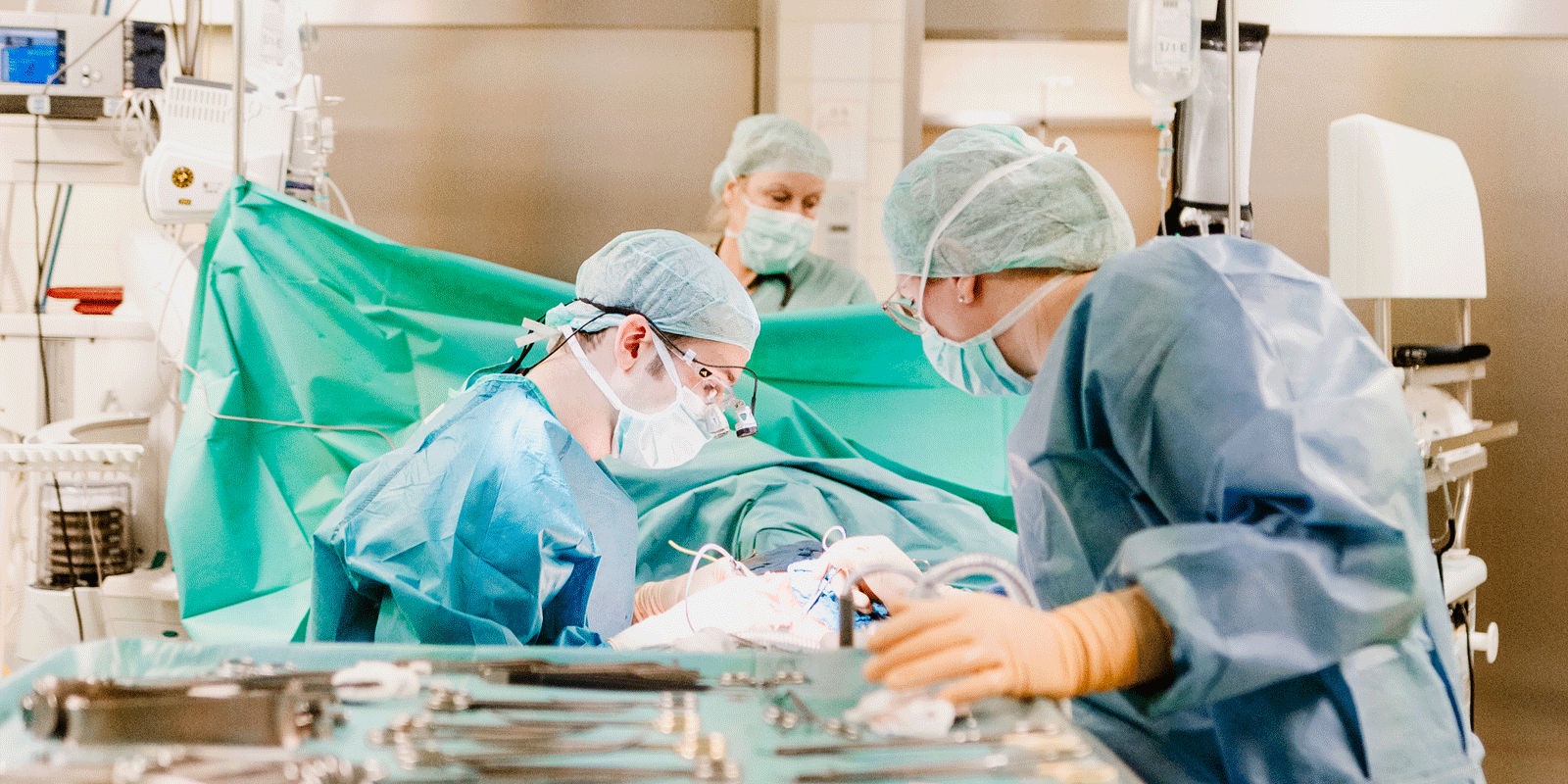 Chirurgen im OP-Saal bei einer Operation, umgeben von medizinischen Geräten und Werkzeugen.