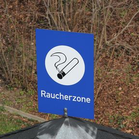 Ein blaues Schild mit der Aufschrift "Raucherzone" und einem Symbol einer brennenden Zigarette.