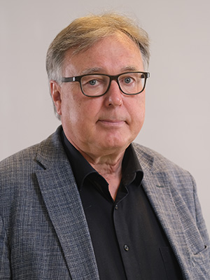 Ein Mann mit Brille und grauem Jackett vor neutralem Hintergrund.