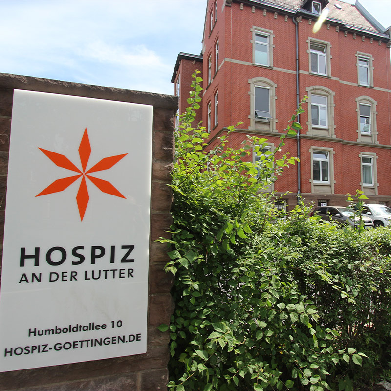 Ein Schild für das Hospiz an der Lutter in Göttingen vor einem Backsteingebäude.