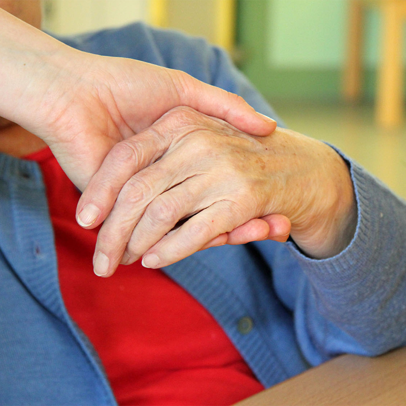 Eine erwachsene Hand hält eine ältere Hand behutsam.