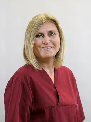 Es zeigt eine lächelnde Frau mit mittellangem blondem Haar in rotem Oberteil vor einem neutralen Hintergrund.