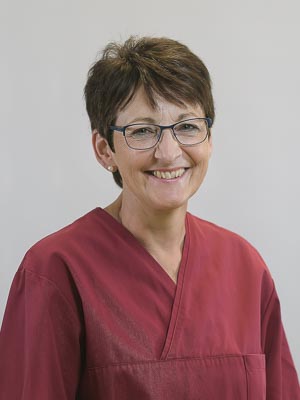 Eine lächelnde Person mit Brille in rotem Oberteil vor einem grauen Hintergrund.