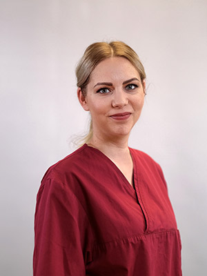 Eine Frau mit blonden Haaren trägt eine rote Bluse vor neutralem Hintergrund.