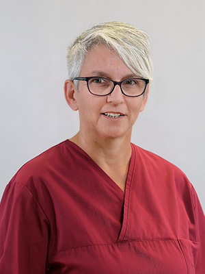 Eine Person mit kurzen grauen Haaren und Brille trägt ein rotes Oberteil vor neutralem Hintergrund.