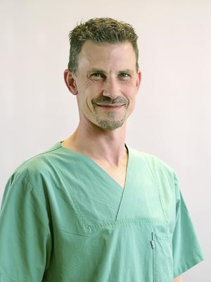 Ein Mann in grünem OP-Kittel lächelt in die Kamera.