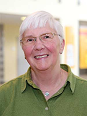 Eine ältere Person mit Brille und grünem Hemd lächelt in die Kamera.