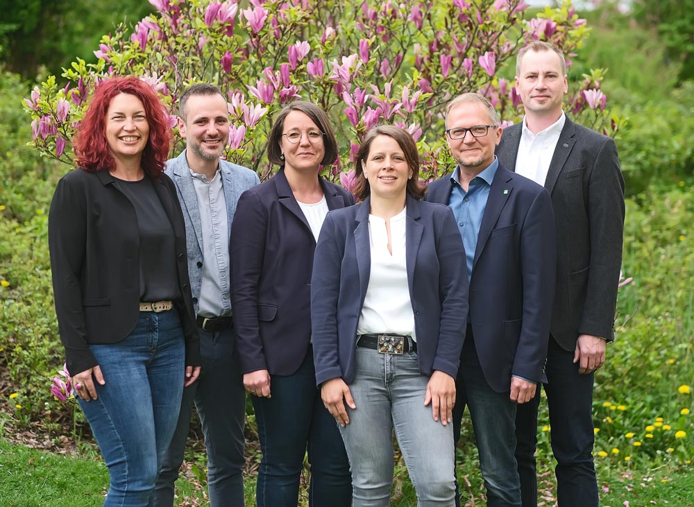 Eine Gruppe von sechs Personen steht vor einem blühenden Magnolienbaum im Freien.